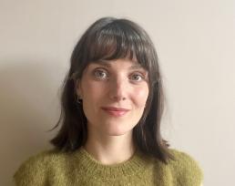 Picture of Lucy Seymour. She has shoulder length brown hair, green eyes and a green top, and white skin.