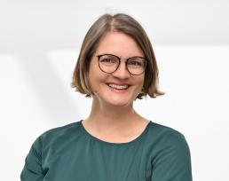 A white woman with a short brown bob and glasses in a dark grey t-shirt.